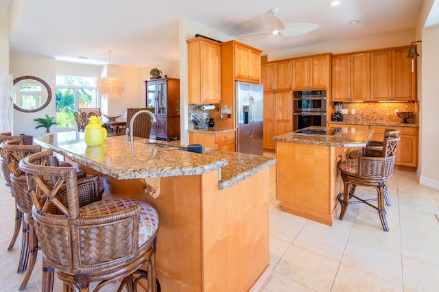 kitchen featuring a kitchen bar, sink, decorative light fixtures, appliances with stainless steel finishes, and a kitchen island with sink