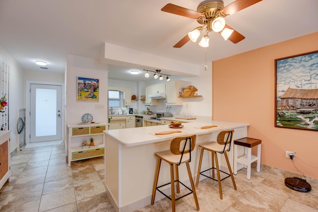 kitchen with washer / clothes dryer, a breakfast bar area, white cabinets, ceiling fan, and kitchen peninsula