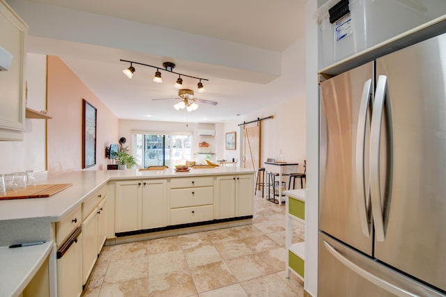 kitchen featuring stainless steel refrigerator, ceiling fan, kitchen peninsula, a barn door, and cream cabinetry