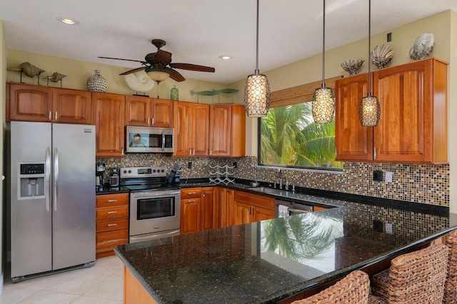 kitchen with sink, decorative light fixtures, dark stone counters, and appliances with stainless steel finishes