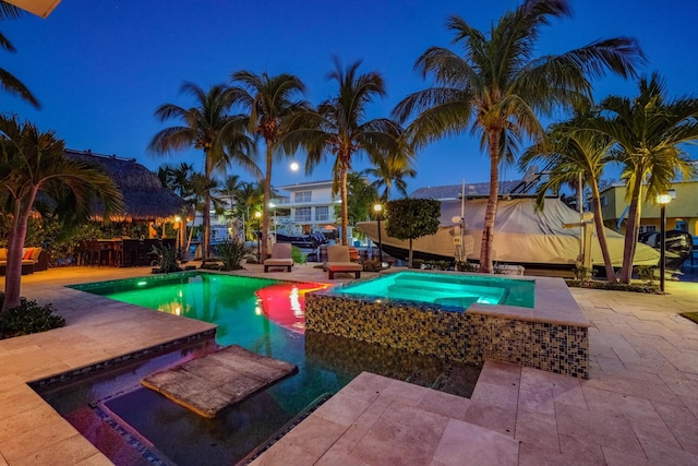 pool at twilight featuring a patio and an in ground hot tub