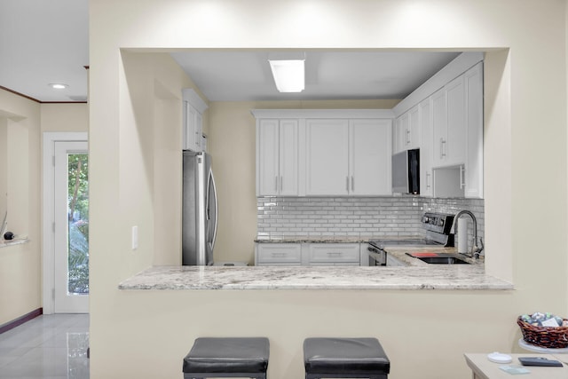 kitchen featuring white cabinetry, backsplash, light stone counters, and stainless steel appliances