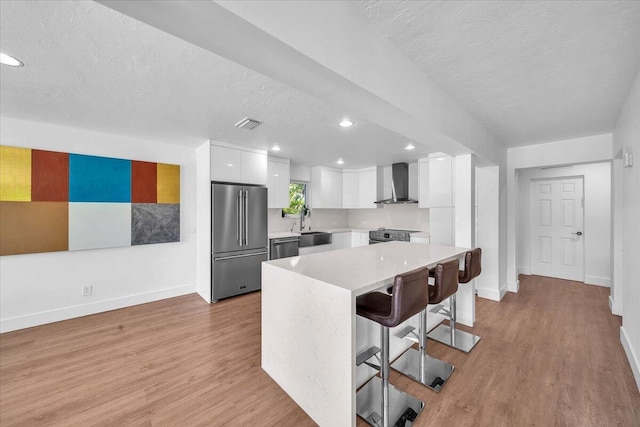 kitchen with a breakfast bar area, white cabinetry, stainless steel appliances, a center island, and wall chimney exhaust hood