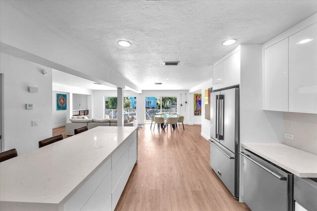 kitchen featuring light hardwood / wood-style flooring, white cabinetry, stainless steel appliances, a center island, and a textured ceiling