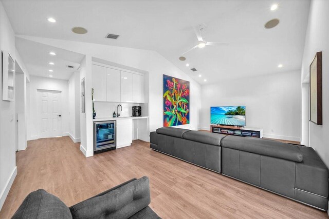 living room featuring vaulted ceiling, light wood-type flooring, wet bar, ceiling fan, and beverage cooler