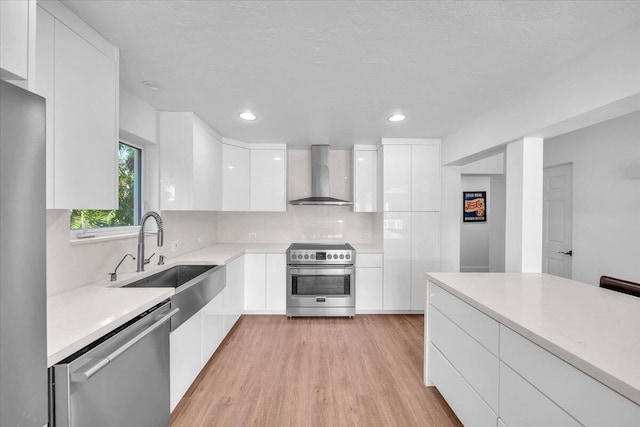 kitchen featuring sink, stainless steel appliances, white cabinets, wall chimney exhaust hood, and light wood-type flooring