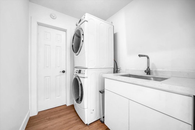 clothes washing area featuring cabinets, stacked washer and clothes dryer, sink, and light wood-type flooring