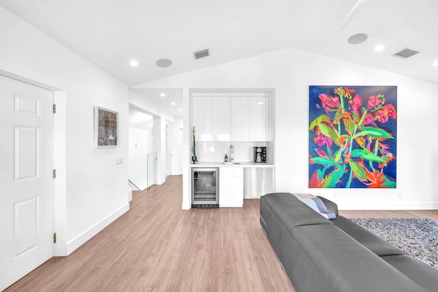 living room with wine cooler, vaulted ceiling, light hardwood / wood-style flooring, and indoor bar