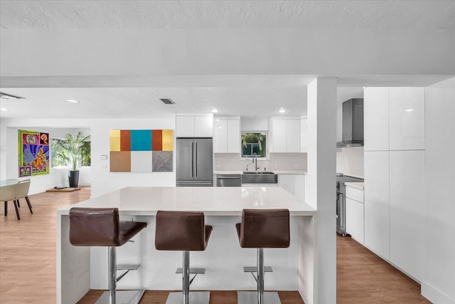 kitchen featuring white cabinetry, appliances with stainless steel finishes, a kitchen breakfast bar, and wall chimney range hood