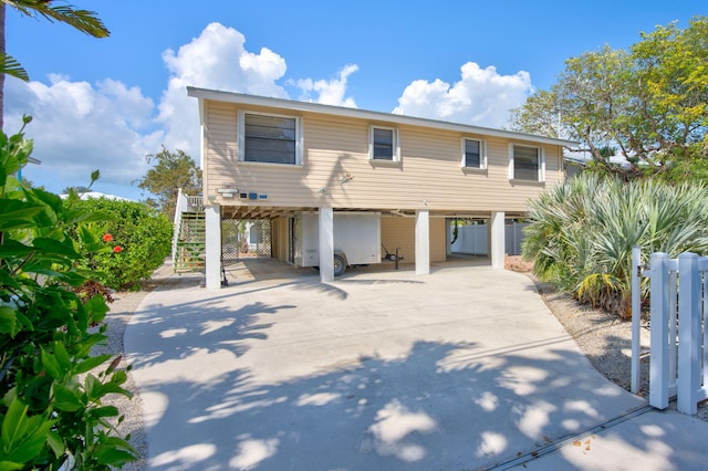 coastal home featuring stairs, a carport, concrete driveway, and fence