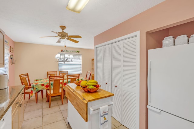 kitchen with white appliances, light tile patterned floors, wooden counters, and ceiling fan with notable chandelier