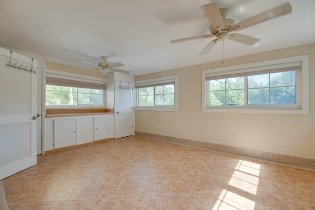 unfurnished room featuring a wealth of natural light, light tile patterned flooring, ceiling fan, and baseboards