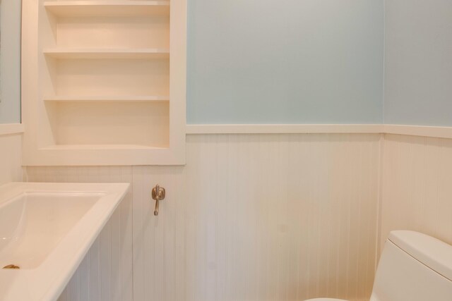 bathroom featuring toilet, built in shelves, and wainscoting