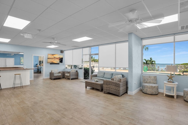 living area with a drop ceiling, a ceiling fan, and light wood finished floors