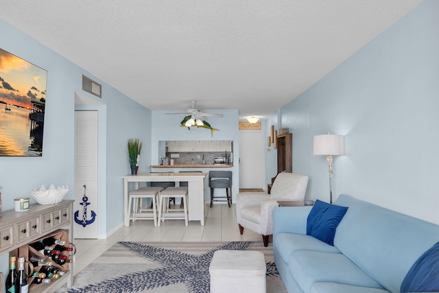 living room featuring tile patterned flooring, visible vents, a textured ceiling, and ceiling fan