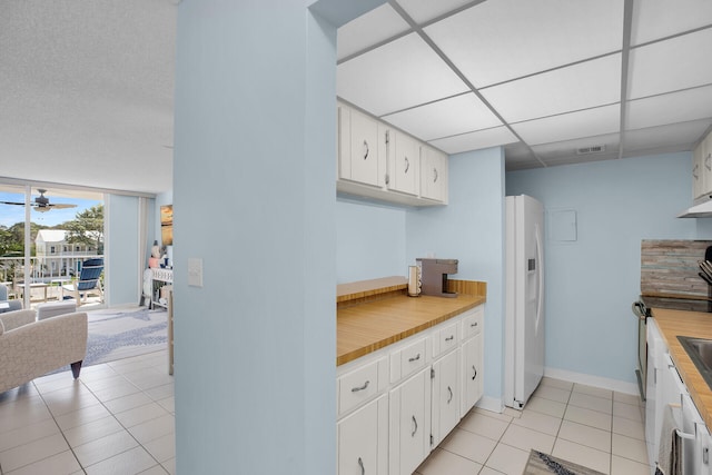 kitchen featuring a ceiling fan, light tile patterned flooring, a drop ceiling, white cabinets, and white refrigerator with ice dispenser