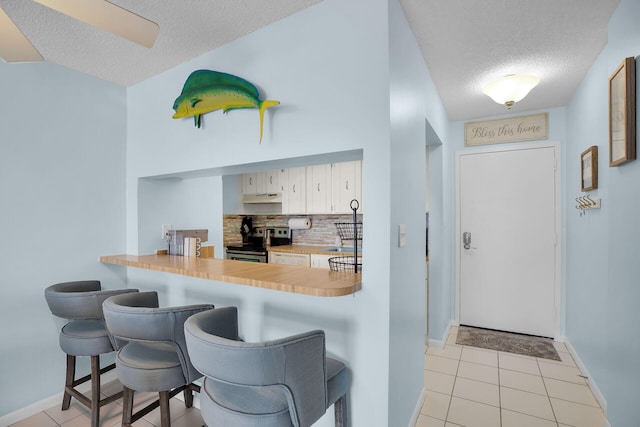 kitchen with light tile patterned floors, stainless steel electric stove, a breakfast bar area, and backsplash