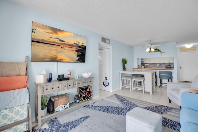 living room with light tile patterned floors, visible vents, a textured ceiling, and a ceiling fan