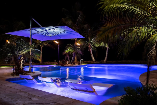 pool at twilight featuring an in ground hot tub