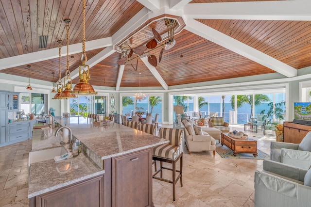 interior space featuring sink, a kitchen island with sink, light stone countertops, decorative light fixtures, and wooden ceiling