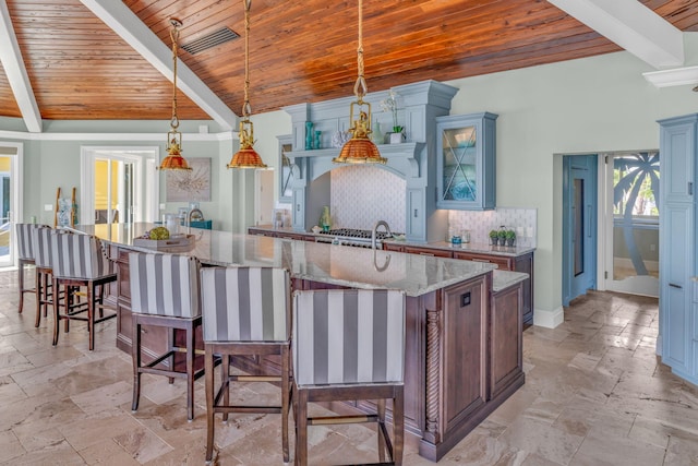 kitchen with light stone countertops, a large island, backsplash, and decorative light fixtures