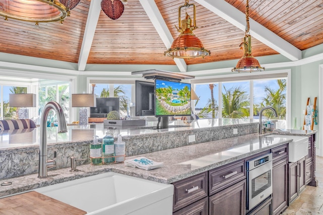 kitchen with sink, beam ceiling, dark brown cabinets, and light stone countertops