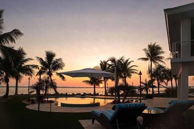 pool at dusk with a water view and a patio