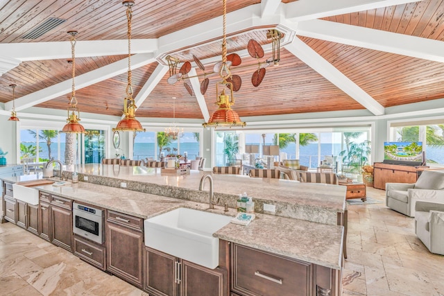 kitchen with light stone counters, a large island, sink, and hanging light fixtures