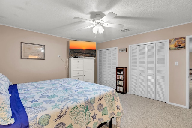 bedroom featuring crown molding, ceiling fan, a textured ceiling, two closets, and light colored carpet