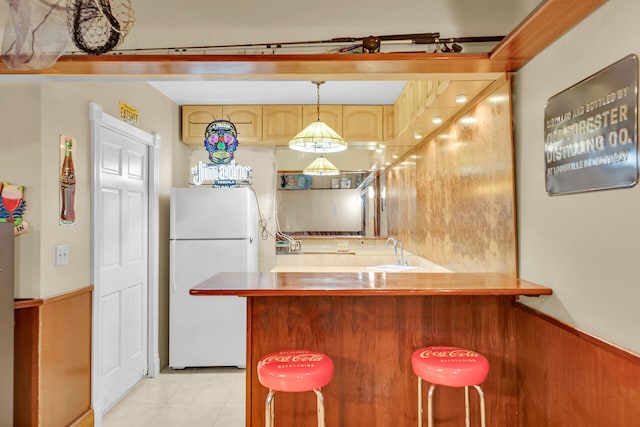 kitchen featuring sink, a breakfast bar area, white refrigerator, decorative light fixtures, and kitchen peninsula