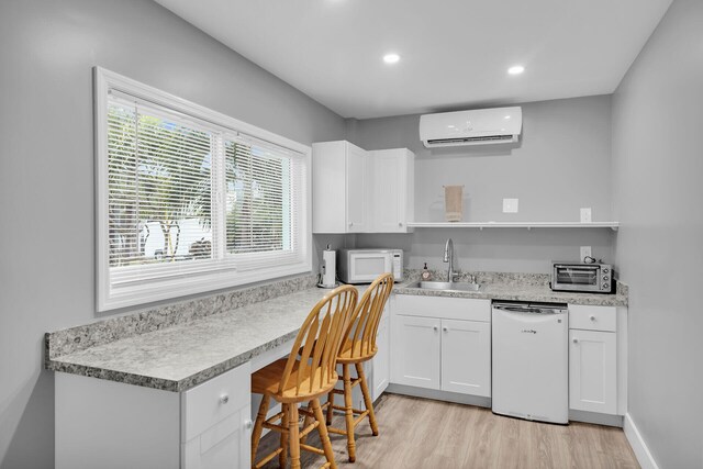 kitchen with sink, white appliances, a wall mounted air conditioner, built in desk, and white cabinets