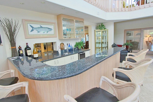 bar featuring stainless steel dishwasher, dark stone counters, light brown cabinetry, and sink