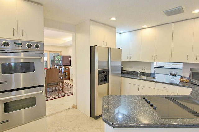 kitchen featuring appliances with stainless steel finishes, sink, dark stone counters, and white cabinets