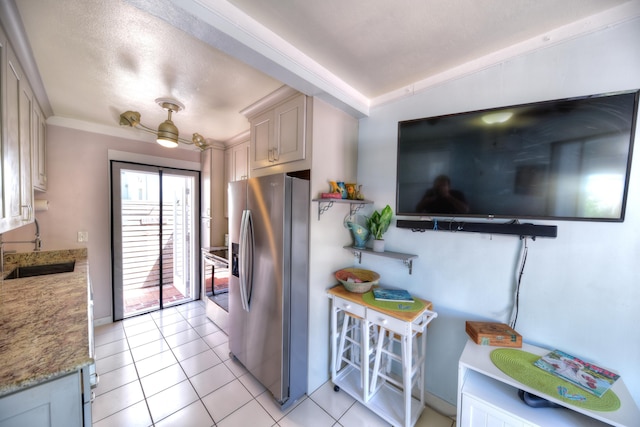 kitchen featuring light tile patterned floors, a sink, ornamental molding, light stone countertops, and stainless steel fridge