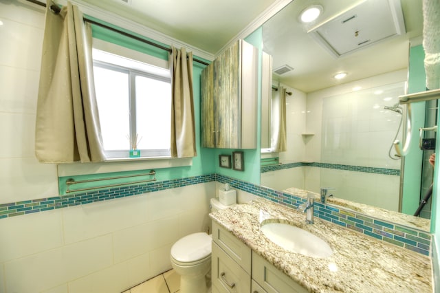 bathroom with visible vents, toilet, a tile shower, vanity, and tile walls