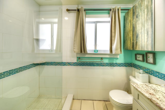 bathroom featuring tile patterned flooring, toilet, vanity, tile walls, and tiled shower