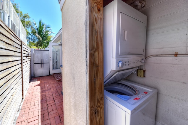 laundry area with laundry area, stacked washer and dryer, wooden walls, and brick floor