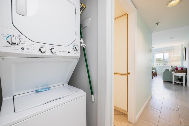 laundry room with light tile patterned floors, stacked washer and dryer, laundry area, and baseboards