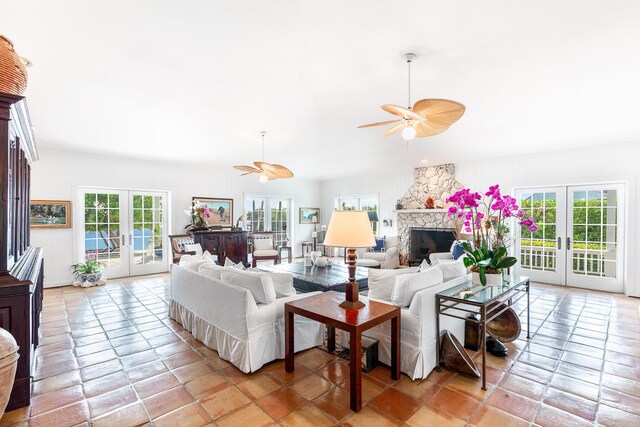 living room featuring a stone fireplace, a wealth of natural light, and french doors