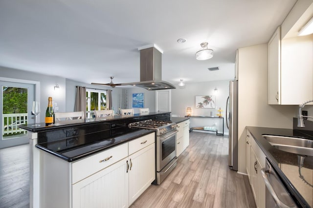 kitchen with appliances with stainless steel finishes, island range hood, sink, white cabinets, and light wood-type flooring