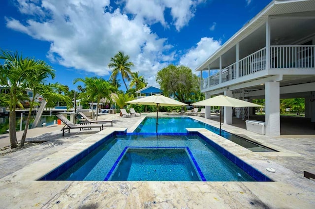 view of pool featuring a patio area, a water view, and an in ground hot tub