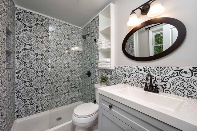 bathroom with tile walls, vanity, tasteful backsplash, a tile shower, and toilet