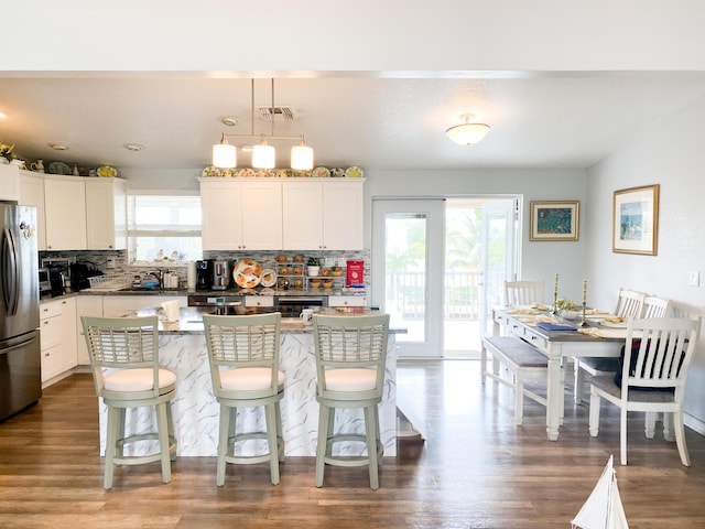 kitchen with pendant lighting, stainless steel fridge, a center island, a healthy amount of sunlight, and white cabinets