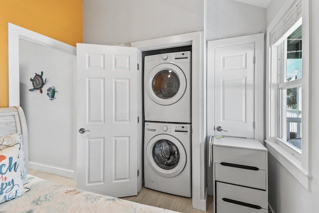 laundry area with stacked washer / drying machine and light hardwood / wood-style flooring