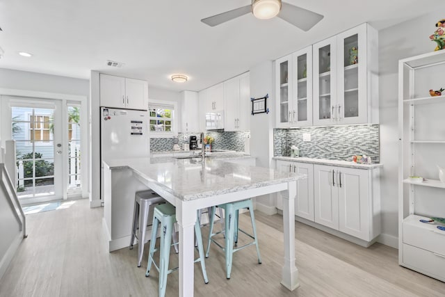 kitchen featuring white cabinets, a kitchen breakfast bar, decorative backsplash, light stone countertops, and white appliances