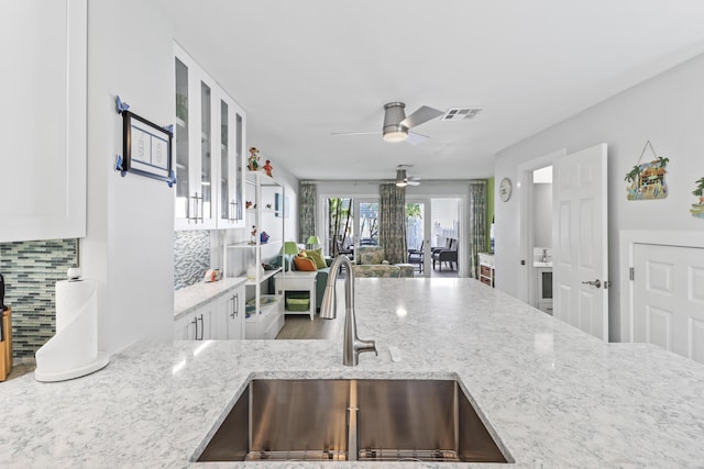 kitchen featuring light stone counters, sink, tasteful backsplash, and white cabinets