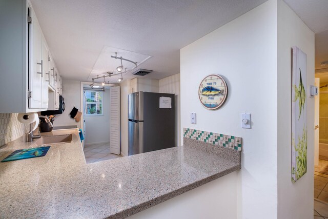 kitchen featuring white cabinetry, sink, stainless steel fridge, and a textured ceiling