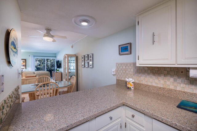 kitchen with tasteful backsplash, white cabinetry, ceiling fan, and light stone counters