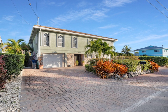 view of front of house featuring stone siding, decorative driveway, an attached garage, and stucco siding