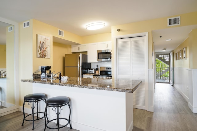 kitchen featuring appliances with stainless steel finishes, white cabinetry, light hardwood / wood-style floors, kitchen peninsula, and dark stone counters